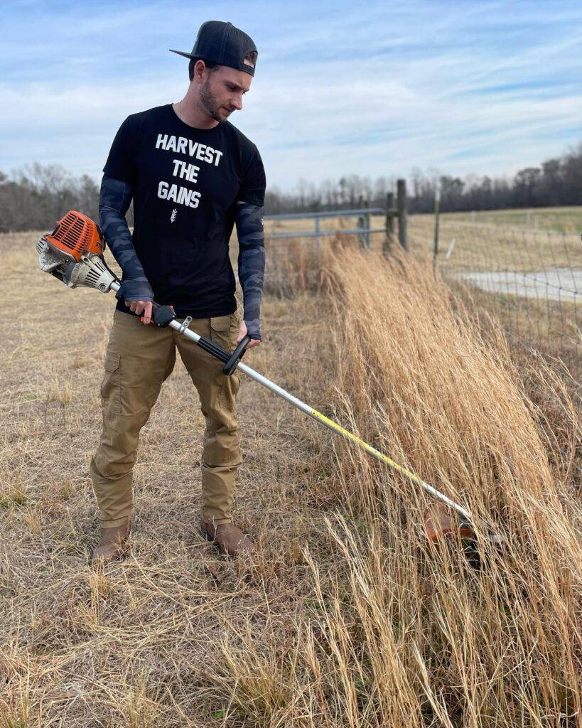 man cutting dried grass with a gas powered grass cutter