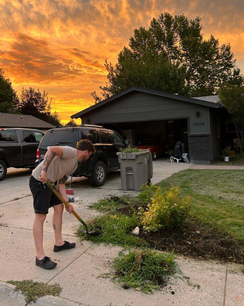 man removing weeds with a shovel beside the driveway