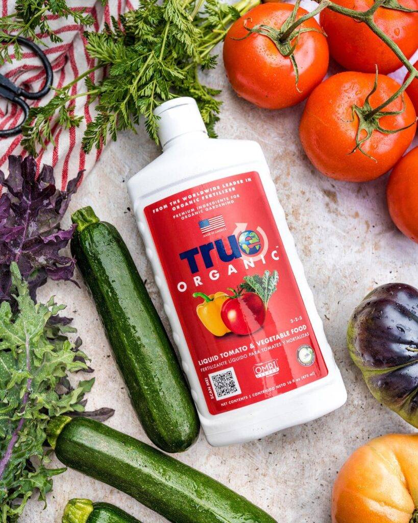 a bottle of true organic liquid fertilizer with cucumbers and tomatoes on the side